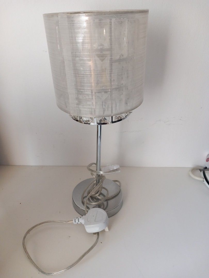 Silver Crystal Shade Table Lamp with Plug （分類：燈飾）位於 Hong Kong。 由 smartwear2ndhand 提交（商品編號 1465904674，圖片 1）。簡介： Bedside table lamp with chrome-finished metal base and stand. Cylindrical fabric shade houses reflective crystal elements inside. Clear power cord attached with standard 3-pin plug. Works great on nightstands, desks, or living room side tables. Clean look, neutral colors match most room decors. Standard bulb socket inside.。