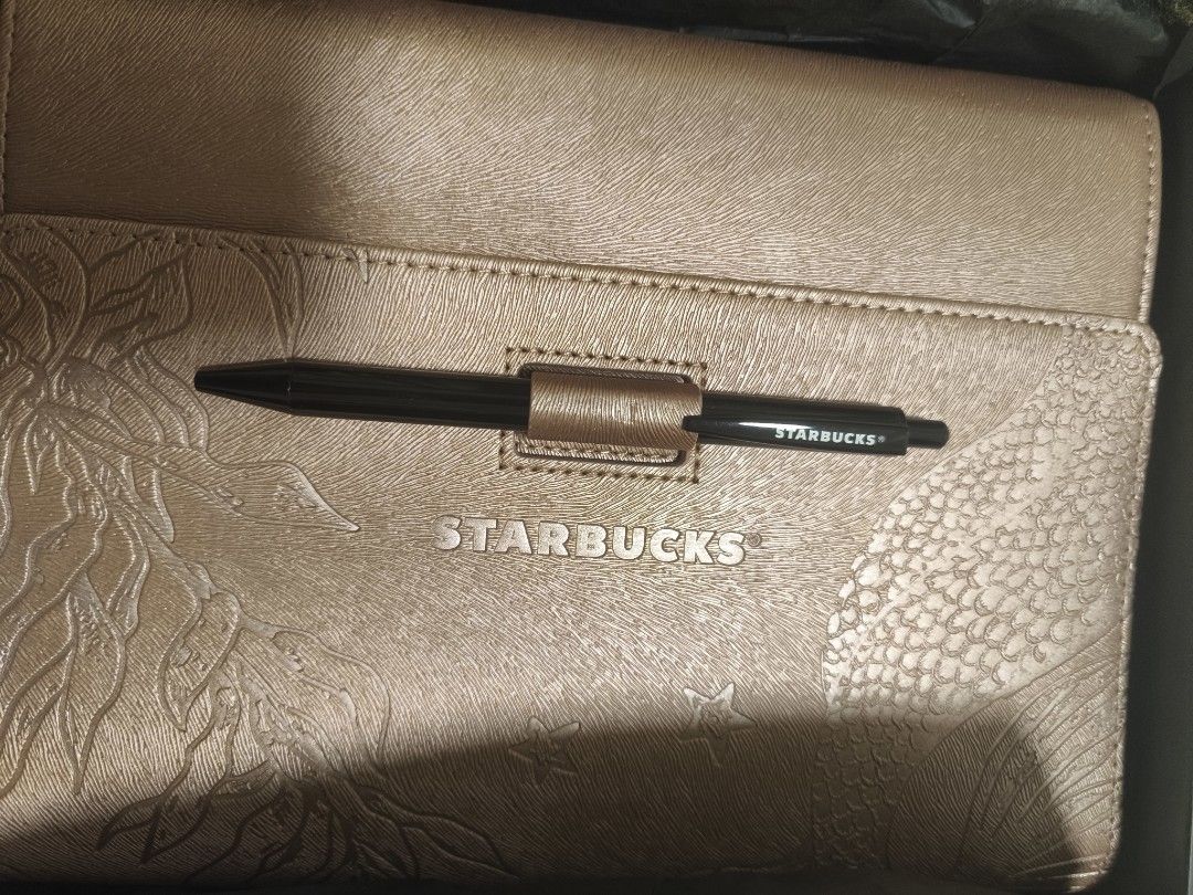 Starbucks Gold Planner 2024 (Category: Stationery & School Supplies) located in Dasmarinas. Submitted by alleethrifthauls (Listing ID 1465822981, Image 2). Description: - Rose gold Starbucks planner in pristine condition - Includes matching black pen and original dark box with Siren logo - Textured cover with elegant mermaid scale and seaweed embossing - Built-in pen holder loop for convenience - Clean and organized layout inside for easy plannin