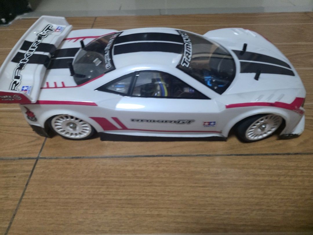 Tamiya Raikiri GT RC Remote Control Drift Car (Category: Remote Control Toys) located in Las Pinas. Submitted by waps05 (Listing ID 1465864231, Image 1). Description: - Style: White body shell with bold black racing stripes and striking pink decals - Aerodynamics: Large rear wing installed for high-speed performance - Wheels & Tires: Multi-spoke white wheels paired with low-profile tires - Interior: Clear windows showcasing internal electronic wi