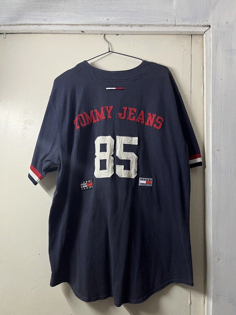 Vintage Tommy Baseball Jersey (Category: Activewear) located in Quezon City. Submitted by GabineteThriftShop (Listing ID 1465863728, Image 3). Description: - Brand: Tommy Jeans - Style: Baseball jersey / Streetwear - Color: Dark navy blue - Size: L - Material: 100% cotton - Origin: Made in Indonesia - Details: Button-down front, striped cuffs, embroidered 'H' chest patch, red stitched 'TOMMY JEANS' lettering, number 85 appliqués, and logo patches