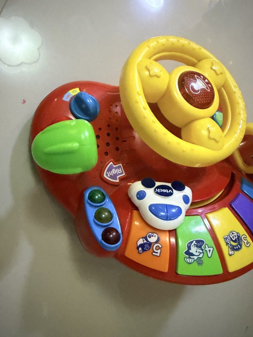 VTech Tiny Tot Driver Interactive Steering Wheel Toy (Category: Infant Playtime) located in San Pablo. Submitted by kimdevera17 (Listing ID 1465857359, Image 2). Description: - VTech interactive toddler steering wheel in bright red and yellow - Features a movable yellow steering wheel with horn button, green gear shifter, traffic lights, and ignition key - Includes a 1-5 piano keyboard with cute animal pictures - Lights and sounds are fully worki