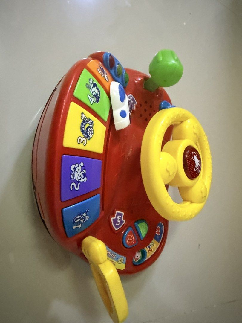VTech Tiny Tot Driver Interactive Steering Wheel Toy (Category: Infant Playtime) located in San Pablo. Submitted by kimdevera17 (Listing ID 1465857359, Image 3). Description: - VTech interactive toddler steering wheel in bright red and yellow - Features a movable yellow steering wheel with horn button, green gear shifter, traffic lights, and ignition key - Includes a 1-5 piano keyboard with cute animal pictures - Lights and sounds are fully worki