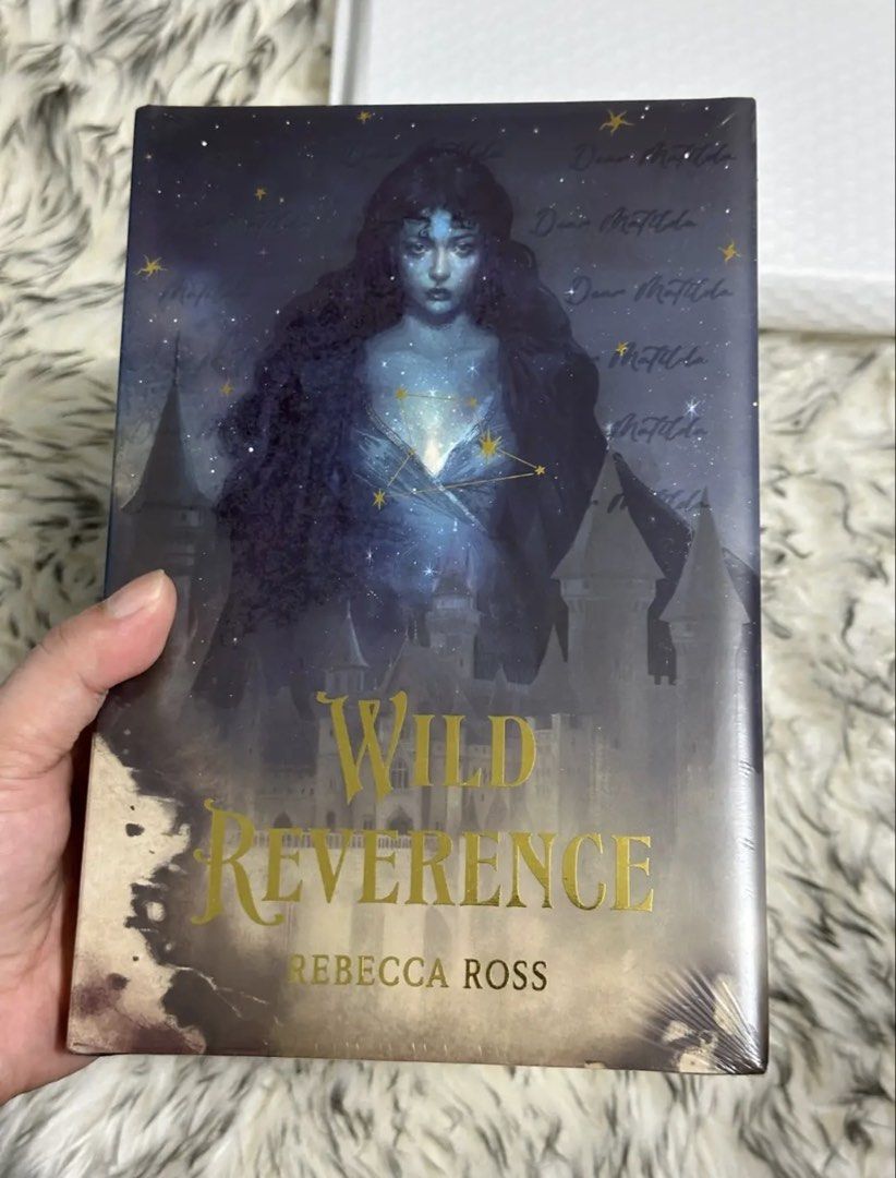 Wild Reverence (Bookish Box ) (Category: Storybooks) located in Manila. Submitted by vivi_rain (Listing ID 1465893481, Image 1). Description: - Title: Wild Reverence by Rebecca Ross - Edition: Bookish Box Edition Hardcover - Condition: Brand new, still in original plastic shrink wrap - Cover Art: Custom design with starry celestial figure and castle details - Back Cover: Handwritten text design reading "Matilda help me" - Edges: Stenciled sprayed