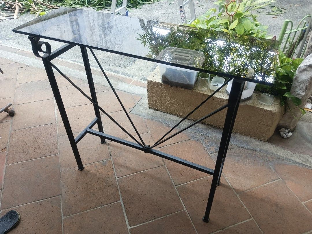 Wrought Iron Console Table with Glass Top (Category: Tables & Sets) located in Pasay City. Submitted by emilsanjose (Listing ID 1465805546, Image 2). Description: - Sleek black metal console table with decorative scrollwork - Tinted glass top and geometric support bars with a wrapped center accent - Sturdy and durable construction, ideal for hallways or entryways - Condition: Good overall with a minor paint chip on one corner near the glass - Col