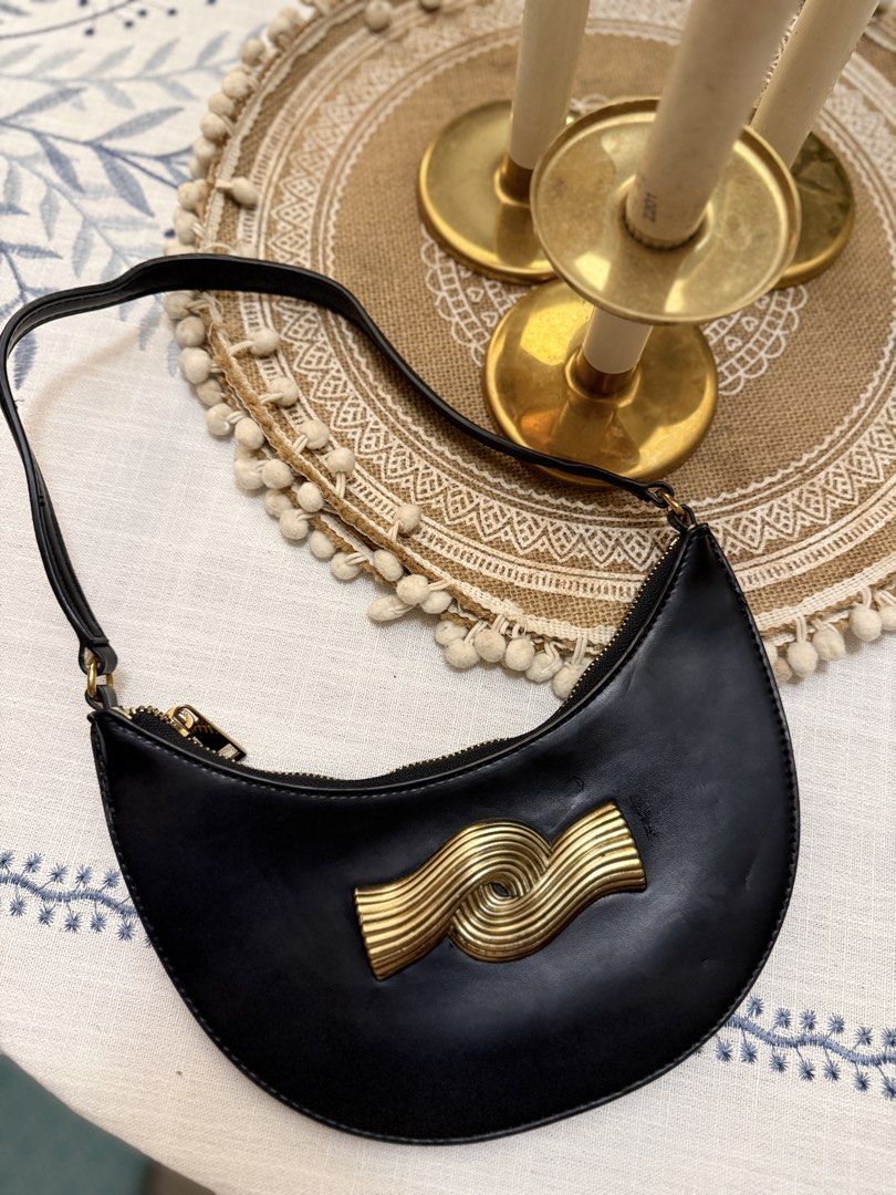 Zara Black Crescent Shoulder Bag with Gold Wave Hardware (Category: Shoulder Bags) located in Quezon City. Submitted by cndcvrtc (Listing ID 1465945401, Image 1). Description: - Style: Black crescent-shaped shoulder bag with clean lines - Design: Features a striking gold metallic wave sculpture on the front - Details: Smooth finish, secure zip top closure, and thin strap - Capacity: Compact size that easily fits your phone and daily essentials - 