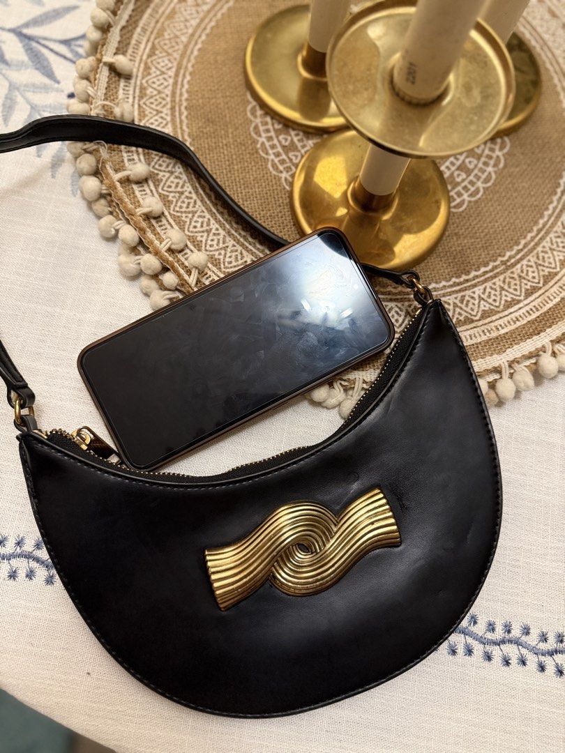 Zara Black Crescent Shoulder Bag with Gold Wave Hardware (Category: Shoulder Bags) located in Quezon City. Submitted by cndcvrtc (Listing ID 1465945401, Image 3). Description: - Style: Black crescent-shaped shoulder bag with clean lines - Design: Features a striking gold metallic wave sculpture on the front - Details: Smooth finish, secure zip top closure, and thin strap - Capacity: Compact size that easily fits your phone and daily essentials - 