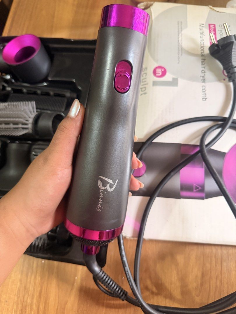 5 in 1 Multifunctional Hair Dryer Comb Styling Tool (Category: Hair) located in Oas. Submitted by joice_29 (Listing ID 1465973621, Image 2). Description: 5-in-1 multifunctional hair styling tool and dryer set by Binnis. Dark grey and pink colorway. Includes main handle with power cord, multiple interchangeable attachments like round brushes, smoothing brush, and drying nozzle. Original packaging box included. Everything neatly fits in the molded 