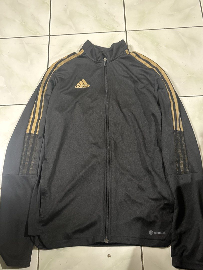 Adidas Tiro Jacket Black Gold (Category: Coats, Jackets and Outerwear) located in Manila. Submitted by uuwoooogghreiri (Listing ID 1466039529, Image 2). Description: - Brand: Adidas Tiro - Color: Black with gold details - Design: Full zip closure, stand-up collar, and classic three stripes on sleeves - Features: Ribbed mesh paneling on upper arms for breathability - Fit: Standard fit, lightweight material - Best for: Workouts, training sessions, 