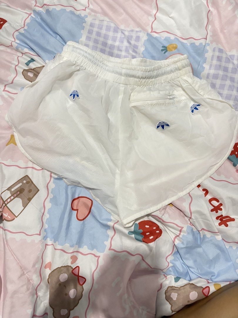 Adidas x Alexander Wang White Shorts (Category: Shorts) located in Makati City. Submitted by jrnhnnh3047116 (Listing ID 1466074465, Image 3). Description: - Brand: Adidas x Alexander Wang - Color: White - Material: Lightweight nylon with comfortable inner mesh lining - Waistband: Elastic drawstring with branded text print and adjustable toggle - Details: Multiple embroidered upside-down trefoil logos on front and back - Pockets: Back zipper pocke