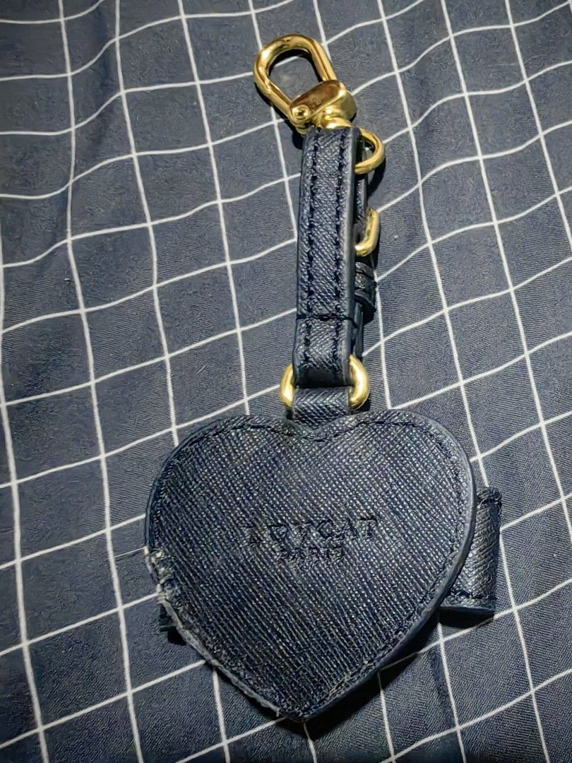LOVCAT Paris Black Heart Bow Bag Charm (Category: Charms) located in Davao. Submitted by thefrugalshop (Listing ID 1466086926, Image 2). Description: - Brand: LOVCAT PARIS - Design: Navy blue textured leather heart charm with a matching bow and gold square accent - Hardware: Gold swivel clasp and adjustable strap buckle at the top - Details: Debossed logo on the back - Condition: Good, with slight fraying along the left edge of the heart - Perfec