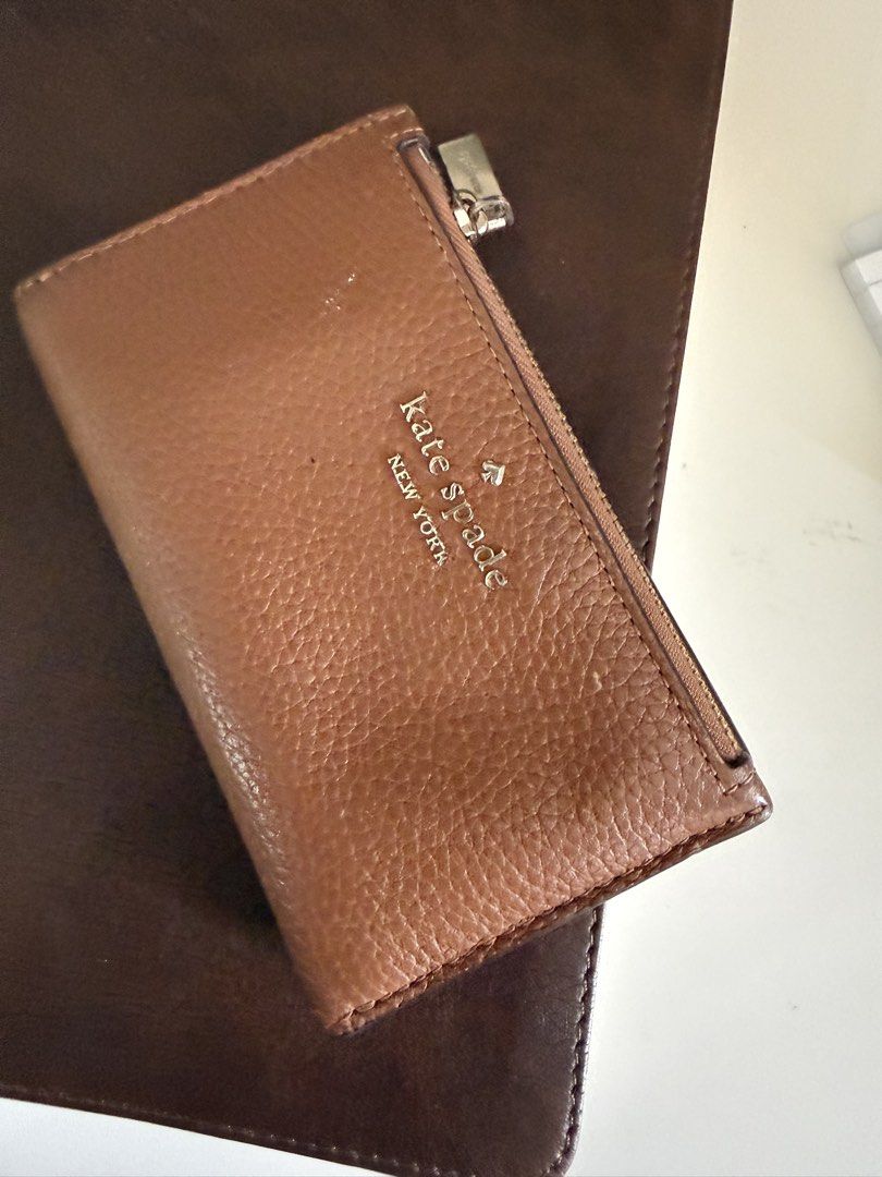 Authentic Kate Spade Bifold Wallet (Category: Wallets & Card holders) located in Marikina City. Submitted by plnkrs (Listing ID 1465990347, Image 1). Description: - Brand: Kate Spade New York - Material: Premium tan pebbled leather - Hardware: Elegant gold-tone with front logo lettering - Exterior: Convenient zip coin pocket - Interior: Multiple card slots, ID window, and signature spade print lining - Closure: Secure snap button closure.