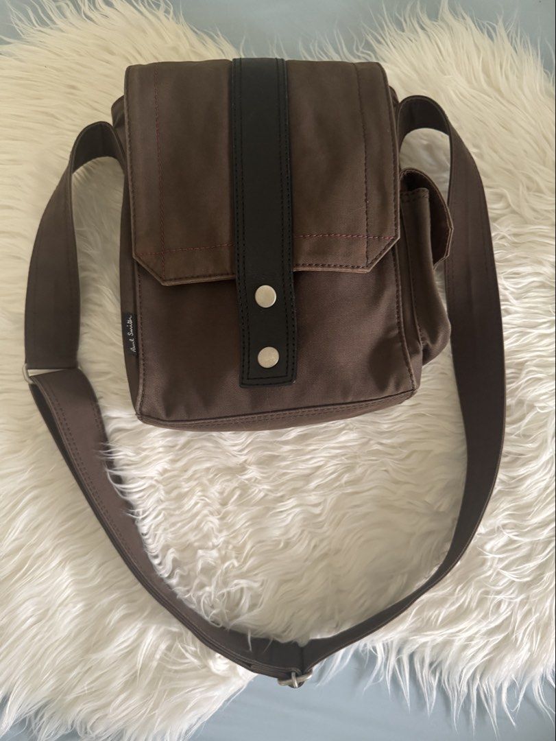 Authentic Paul Smith Brown Canvas Crossbody Bag with Adjustsble Strap (Category: Sling Bags) located in Pasig City. Submitted by topbrandpursuits (Listing ID 1465804920, Image 2). Description: - Authentic Paul Smith crossbody bag in durable brown canvas - Features a striking vertical black leather center stripe - Eye-catching contrast pink stitching on the front flap and side pocket - Convenient side pocket with velcro closure - Adjustable brown 