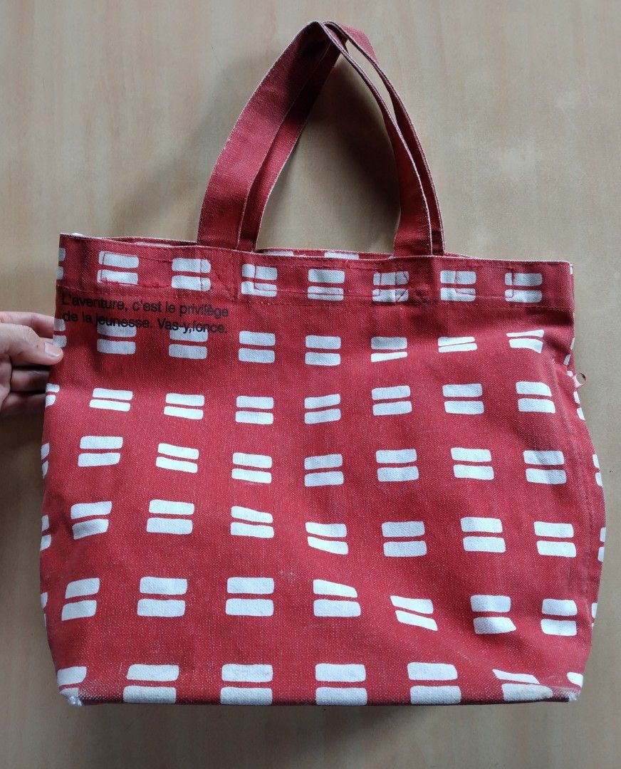 Avion De Papier Red Patterned Thick Canvas Tote Bag (Category: Tote Bags) located in Baguio. Submitted by tipiditis (Listing ID 1466030344, Image 1). Description: - Red canvas tote bag with a white geometric pattern and French phrase - Dual top handles for easy carrying - Roomy interior equipped with multiple slip pockets - Secure built-in zipper closure along the side gusset - Sturdy exterior fabric construction - Flaw: Interior lining has visib