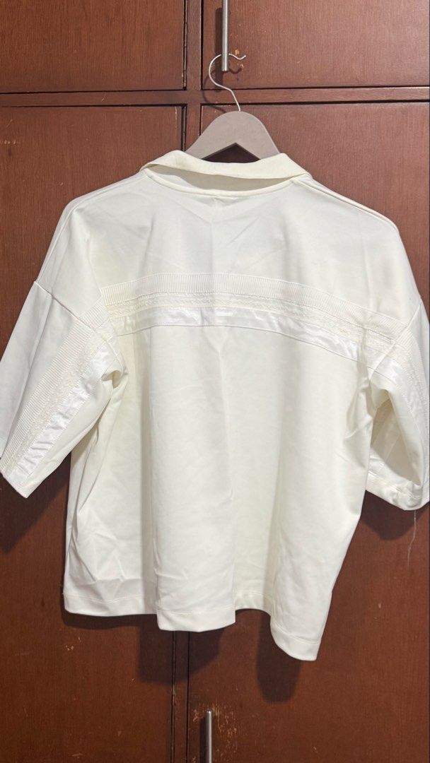 B+ab White Cropped Polo Shirt (Category: Tshirts & Polo Shirts ) located in Pasig City. Submitted by 35th.store (Listing ID 1466152851, Image 3). Description: - Brand: b+ab - Style: Short sleeve polo shirt with collared neck and front buttons - Size: Medium but can fit to Large - Material: 97.7% polyester, 2.3% spandex (slightly stretchy and easy to wear) - Design details: Textured trim across the chest and shoulders with cute ribbon detail, plus