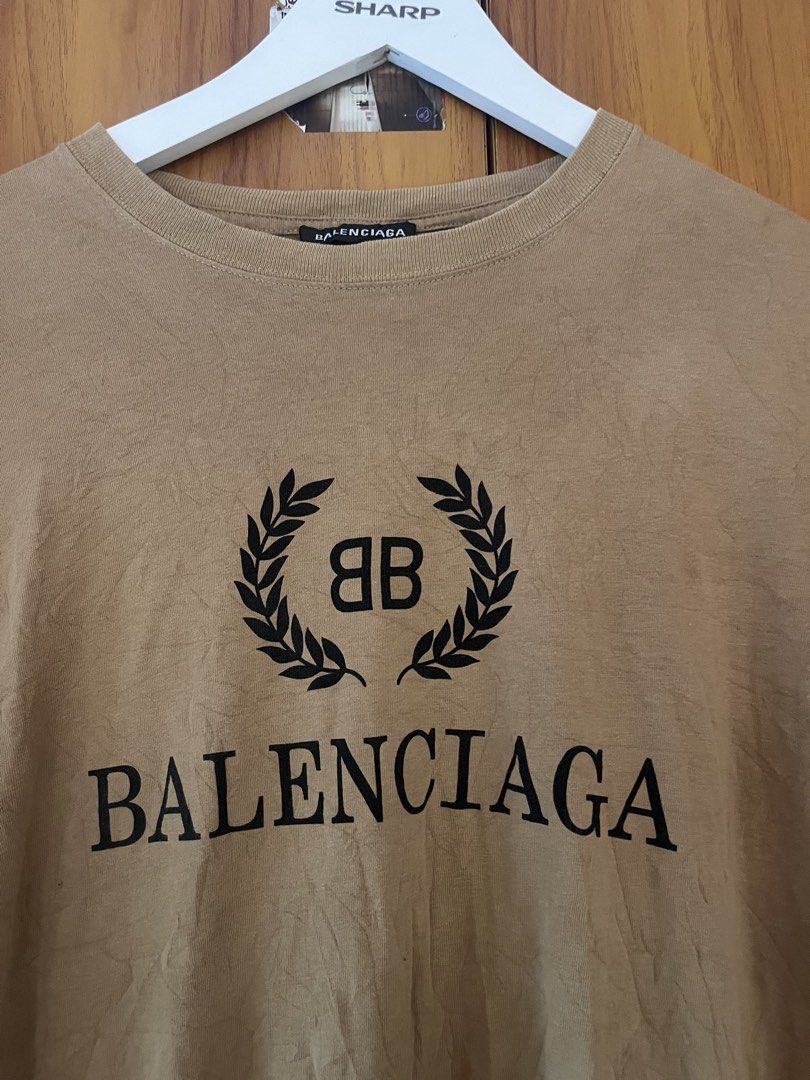Balenciaga Laurel Wreath Logo Tee Brown Medium (Category: Luxury Apparel) located in Manila. Submitted by christian048 (Listing ID 1466096633, Image 3). Description: - Brand: Balenciaga - Color: Brown with black logo - Design: Large laurel wreath print on chest - Fit: Oversized with drop shoulders - Size: Medium (tag on collar) - Material: 100% Cotton - Origin: Made in Portugal - Condition: Minor wrinkling from storage, needs a quick iron or stea