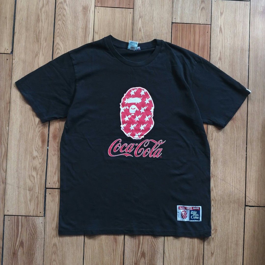 BAPE x Coca-Cola Black T-shirt (Category: Shirts) located in Paranaque City. Submitted by thriftine5 (Listing ID 1466009543, Image 1). Description: - Authentic BAPE x Coca-Cola collaboration t-shirt - Color: Classic Black - Material: Comfortable 100% Cotton - Front design: Iconic ape head filled with red star and lightning bolt graphics, plus Coca-Cola branding and woven hem tag - Back design: 'the Real Thing!' and 'A Bathing Ape' lettering - Det