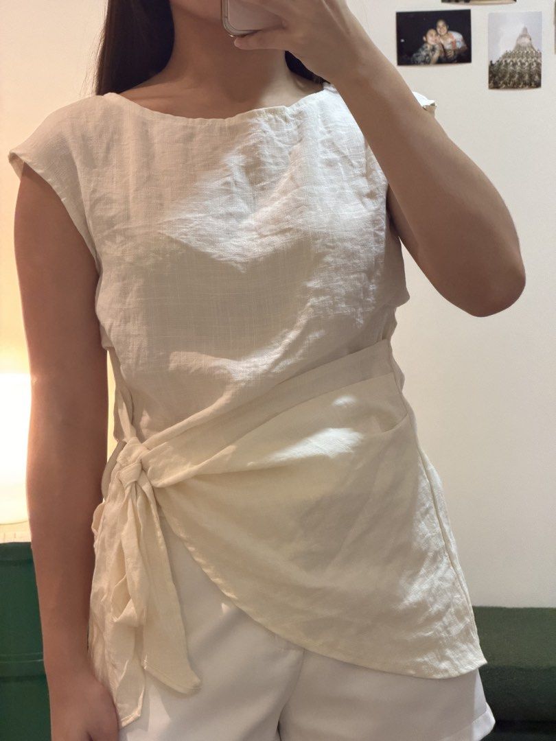 Beige Linen Wrap Blouse Sleeveless Top (Category: Blouses) located in Cebu City. Submitted by wearhousebyhya (Listing ID 1466023228, Image 3). Description: - Color: Neutral beige - Material: Lightweight and breathable linen - Design: Sleeveless with a structured boat neckline - Detail: Wrap-around front panel with a side bow - Hem: Trendy asymmetrical cut - Fit: Versatile and perfect for warm weather.