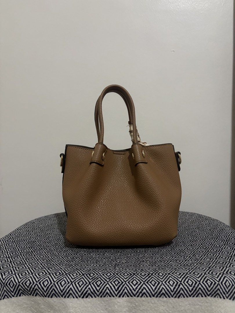 Bessie London Hand Bag with Strap (Category: Tote Bags) located in Makati City. Submitted by allaineallaine (Listing ID 1466115067, Image 3). Description: Bessi London Handbag - Rich brown pebble-textured finish with elegant gold-tone hardware - Versatile carrying options: dual top handles and a detachable shoulder strap - Chic matching patterned scarf included on the handle - Organized interior with a central zippered compartment and secure magn