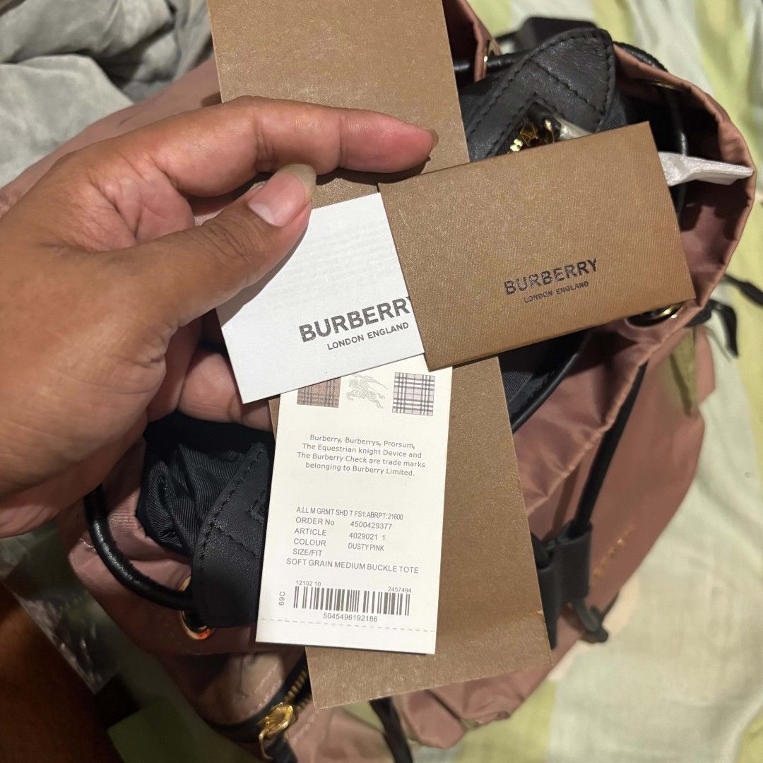 Burberry The Rucksack Cloth Backpack Dusty Pink (Category: Backpacks) located in Carmen. Submitted by ar_thrift00 (Listing ID 1466088608, Image 2). Description: - Brand new with original tags attached - Color/Material: Dusty pink nylon cloth with black leather trim - Hardware: Elegant gold-tone accents - Closure: Secure drawstring with top buckle flap - Pockets: Front zip pocket, two side zip pockets, and interior zip pocket - Interior: Features 