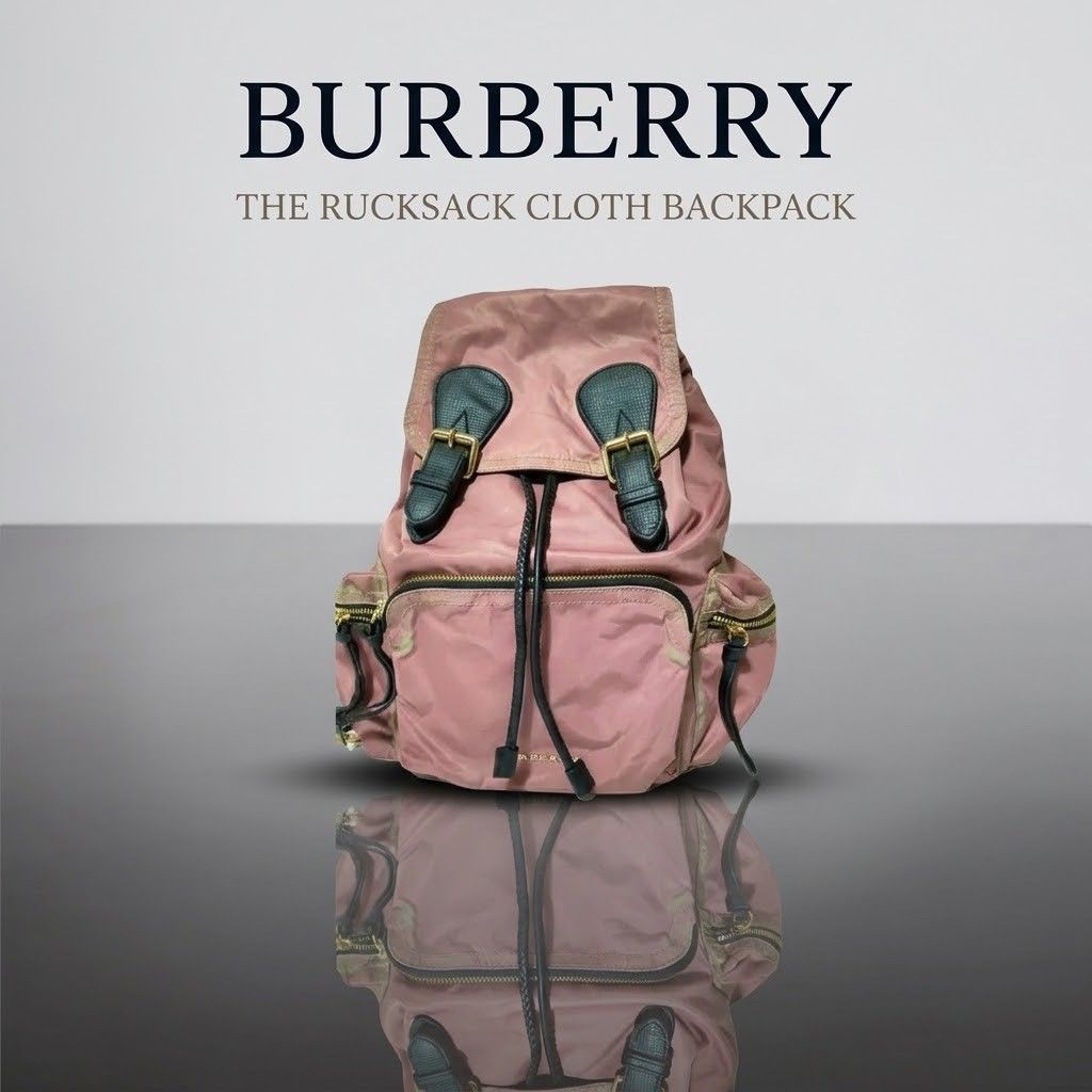 Burberry The Rucksack Cloth Backpack Dusty Pink (Category: Backpacks) located in Carmen. Submitted by ar_thrift00 (Listing ID 1466088608, Image 1). Description: - Brand new with original tags attached - Color/Material: Dusty pink nylon cloth with black leather trim - Hardware: Elegant gold-tone accents - Closure: Secure drawstring with top buckle flap - Pockets: Front zip pocket, two side zip pockets, and interior zip pocket - Interior: Features 