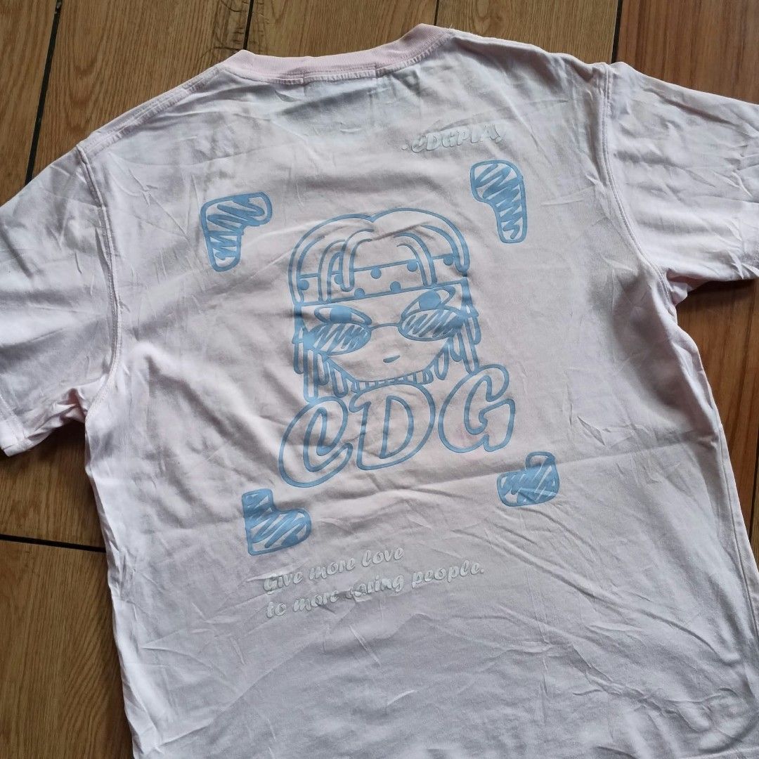 CDG Play Pink Graphic T-Shirt (Category: Shirts) located in Paranaque City. Submitted by thriftine5 (Listing ID 1466010708, Image 3). Description: Light pink graphic tee from CDG Play. Small embroidered red and blue heart patches on the chest. Large cartoon graphic and typography printed on the back. Crew neck, short sleeves. Has a noticeable faint stain on the front lower chest area..