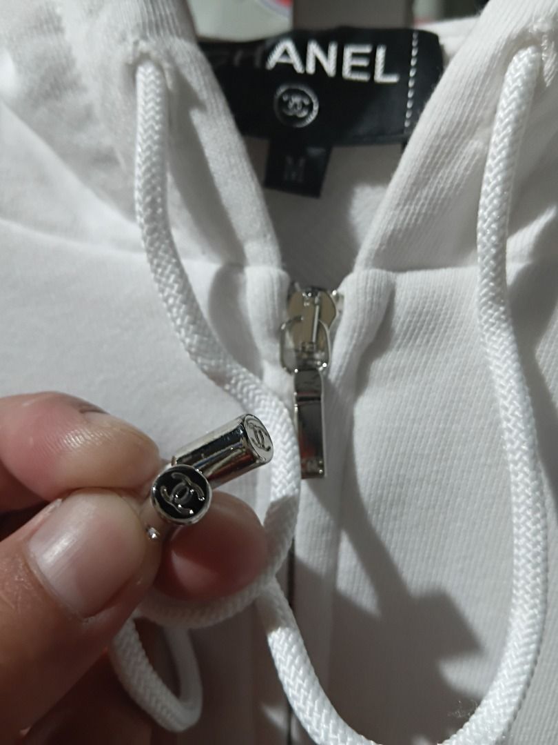 Chanel cambon zip up hoodie (Category: Hoodies) located in Caloocan City. Submitted by allen_09191996 (Listing ID 1465964794, Image 3). Description: - Color: White with striking black graphic collage on the back - Design: Features Chanel branding, camellia motifs, and Coco lettering - Size: M (tagged at collar) - Material: Soft, comfortable cotton-blend fabric with a clean finish - Hardware: Silver-tone throughout, including a branded zip pull an
