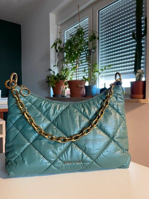 CHARLES & KEITH Puffy Quilted Chain Handle Bag (Category: Shoulder Bags) located in Manila. Submitted by vibevault.ph (Listing ID 1465982944, Image 2). Description: • Color is sage green in real life, but the camera couldn’t capture its true color accurately due to the lighting. • Versatile and can be worn in different ways — remove the strap to use it as a shoulder bag, or wear it as shown in the first photo. • RFS: Need funds and realized the c