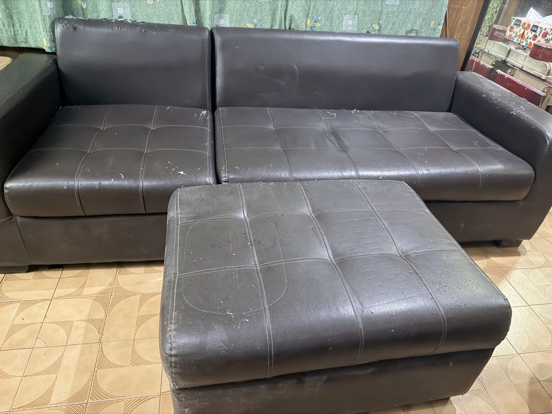 Dark brown leather sectional sofa with matching ottoman (Category: Sofas) located in Quezon City. Submitted by BAYMAX72 (Listing ID 1465975575, Image 1). Description: - Dark brown faux leather sectional sofa with matching footstool ottoman - Elegant tufted cushioning on seats and ottoman - Solid and sturdy internal structure - Noticeable wear and tear from pet scratches on arms, top edges, and seating surfaces - Fully functional and ready for use