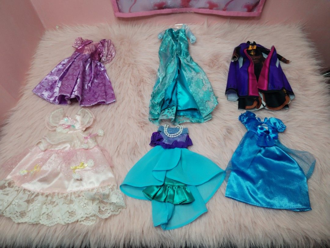 Disney Princess Doll Dresses (Category: Kids Toys) located in Paombong. Submitted by eandj.shop (Listing ID 1466053046, Image 3). Description: 🎀 Set of 6 stunning doll dresses 🎀 Variety of styles: Purple sparkly gown, light blue glitter ice dress, purple/black cape outfit, pink satin dress with lace, turquoise high-low dress with pearls, and bright blue satin dress 🎀 Perfect for playtime, dress-up, and expanding your doll's wardrobe.