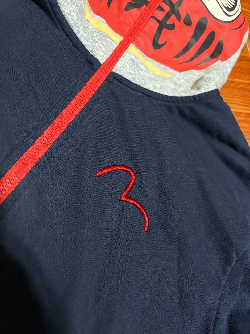 Evisu Heritage Daruma Hooded Zip Jacket Navy Red (Category: Coats, Jackets and Outerwear) located in Manila. Submitted by lancee1208 (Listing ID 1466061953, Image 3). Description: - Brand: Evisu Heritage - Color: Dark blue with bold red accents - Design: Full red front zipper and matching red gull embroidery on the chest - Unique Feature: Hood unzips entirely to reveal a large Daruma doll face graphic inside and out - Details: Red and white strip