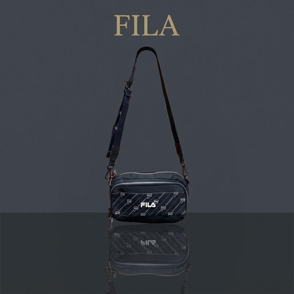 Fila Crossbody Bag (Category: Cross-body Bags) located in Carmen. Submitted by ar_thrift00 (Listing ID 1466085108, Image 1). Description: - Brand: Fila - Color: Navy blue with white logo prints and diagonal stripe patterns - Strap: Adjustable with metal eyelets and side clips - Interior: Fabric lining with brand tags and serial number labels - Closure: Zipper closures with braided red, white, and black pull cords - Condition: Minor wear near the 