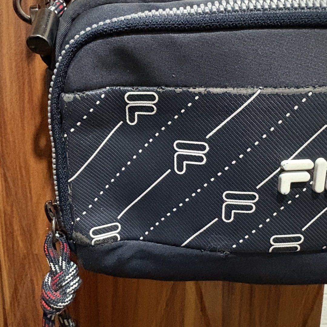 Fila Navy Blue Crossbody Bag with Monogram Pattern (Category: Cross-body Bags) located in Carmen. Submitted by rr_thrifts (Listing ID 1466033954, Image 3). Description: - Brand: Fila - Color: Navy Blue with white monogram pattern - Style: Compact crossbody / sling bag with multi-zip compartments - Hardware: Sturdy dark metal clasps and smooth zippers with decorative pull cords - Strap: Adjustable fabric strap featuring stylish metal eyelets - Con