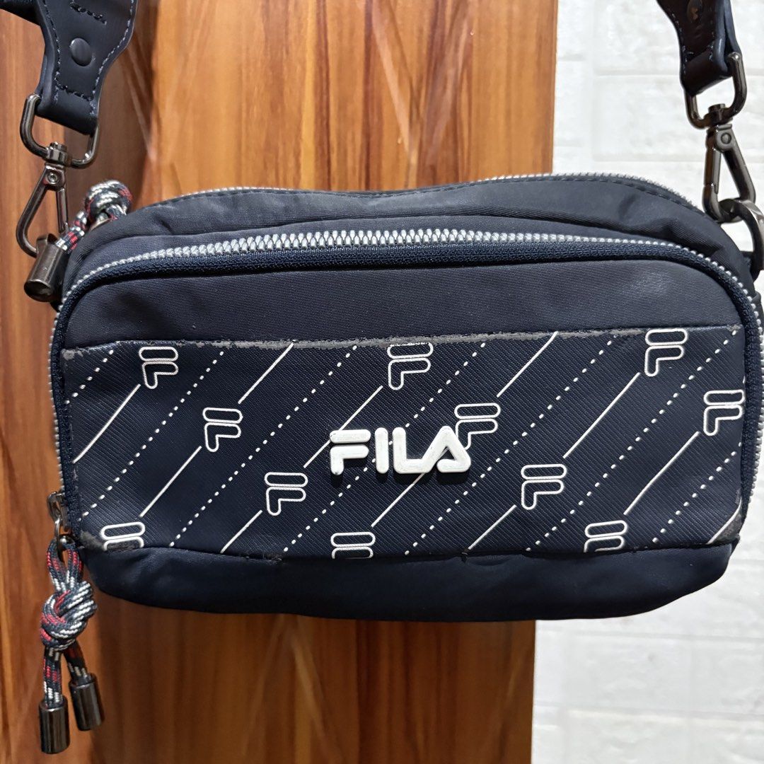 Fila Navy Blue Crossbody Bag with Monogram Pattern (Category: Cross-body Bags) located in Carmen. Submitted by rr_thrifts (Listing ID 1466033954, Image 2). Description: - Brand: Fila - Color: Navy Blue with white monogram pattern - Style: Compact crossbody / sling bag with multi-zip compartments - Hardware: Sturdy dark metal clasps and smooth zippers with decorative pull cords - Strap: Adjustable fabric strap featuring stylish metal eyelets - Con