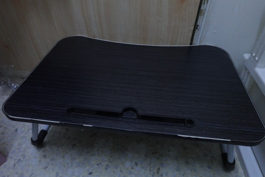 Foldable Small Table (Category: Tables & Sets) located in Kuala Lumpur. Submitted by vyeas (Listing ID 1466024983, Image 2). Description: - Size: 39cm × 60cm - Portable lap desk with a stylish black wood-grain surface - Built-in slot conveniently holds tablets and phones upright - Sturdy foldable metal legs with rubber feet for a secure grip on beds, floors, or couches - Ergonomic curved front edge for comfortable seating - Condition: lightly use