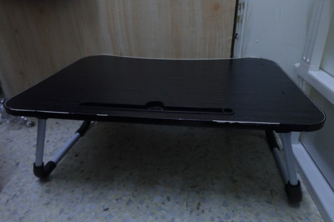 Foldable Small Table (Category: Tables & Sets) located in Kuala Lumpur. Submitted by vyeas (Listing ID 1466024983, Image 1). Description: - Size: 39cm × 60cm - Portable lap desk with a stylish black wood-grain surface - Built-in slot conveniently holds tablets and phones upright - Sturdy foldable metal legs with rubber feet for a secure grip on beds, floors, or couches - Ergonomic curved front edge for comfortable seating - Condition: lightly use