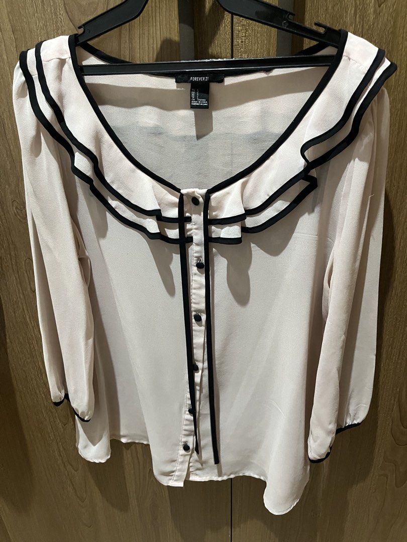Forever 21 Ruffle Collar Blouse Size L (Category: Blouses) located in Quezon City. Submitted by epictiger.c6451a (Listing ID 1465963760, Image 1). Description: - Brand: Forever 21 - Size: L (tag attached) - Color: Light pink with black trim - Design: Double ruffle collar, button-up front, long sleeves with trimmed cuffs - Material: Lightweight fabric - Origin: Made in China - Condition: Excellent/Ready to wear - Versatility: Perfect for both work