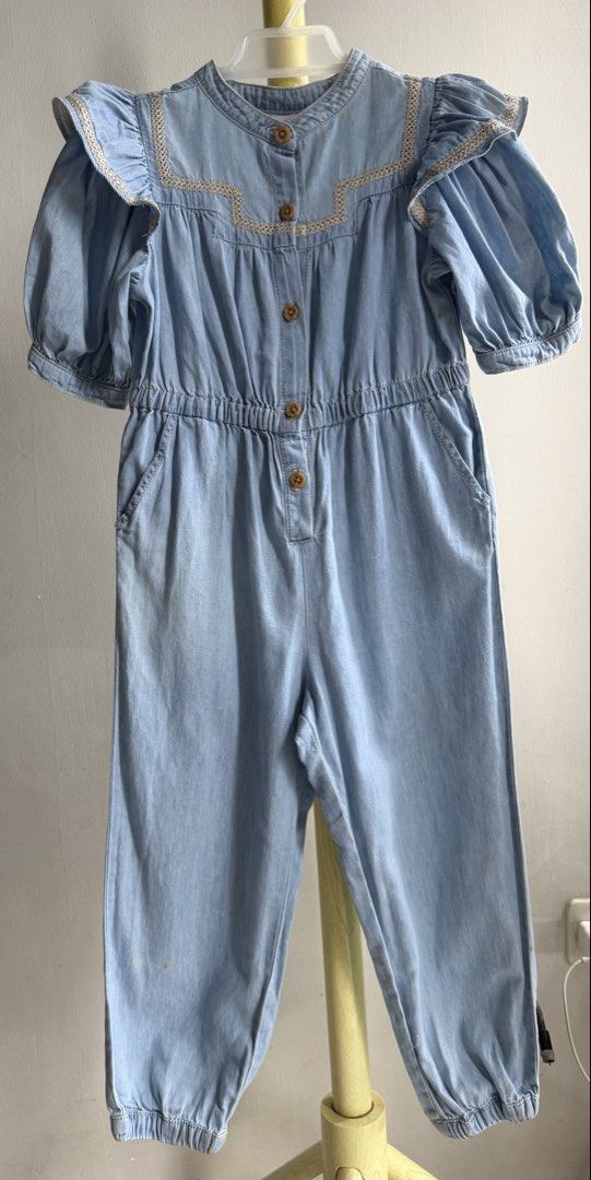 Gingersnaps Denim Jumpsuit Size 4 (Category: Babies & Kids Fashion) located in Quezon City. Submitted by warmrabbit_414908 (Listing ID 1465985995, Image 3). Description: - Brand: Gingersnaps - Size: 4 years - Color: Light blue - Material: Lightweight chambray - Design: Short puff sleeves with ruffled shoulders and chest embroidery - Features: Front button closure with wooden-look buttons, elastic waistband, side pockets, and elastic ankle cuffs -
