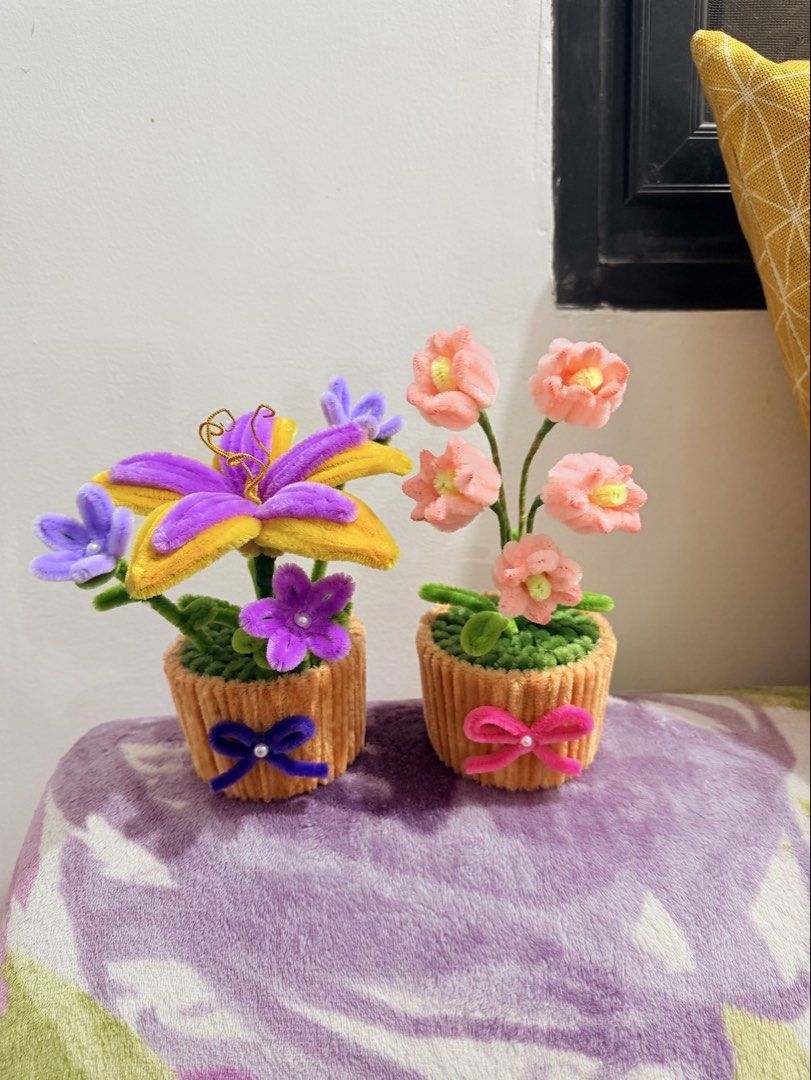 Handmade Flower Pot Decorative Craft (Category: Handmade Craft) located in Dasmarinas. Submitted by ligean2738954 (Listing ID 1466108002, Image 3). Description: - Handmade pipe cleaner floral craft set featuring two small potted bases - Left pot includes a large purple and yellow lily with smaller purple blossoms - Right pot features several delicate pink blossoms on stems - Beautifully wrapped in textured fabric with a matching ribbon bow and pe