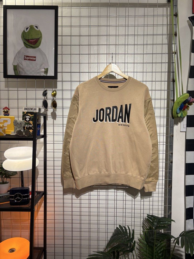 Jordan Beige Sweatshirt with Black Lettering (Category: Coats, Jackets and Outerwear) located in Cavite. Submitted by vlblgrmnts_ (Listing ID 1466076627, Image 1). Description: Jordan - P235 23x27 Bestfit Large 9/10 CR 900 Jordan crewneck sweatshirt in a tan beige colorway. Bold black JORDAN text printed on the chest along with a net weight detail. Ribbed collar featuring red and white stripes inside. Standard cuffs and hem. Classic piece for cas
