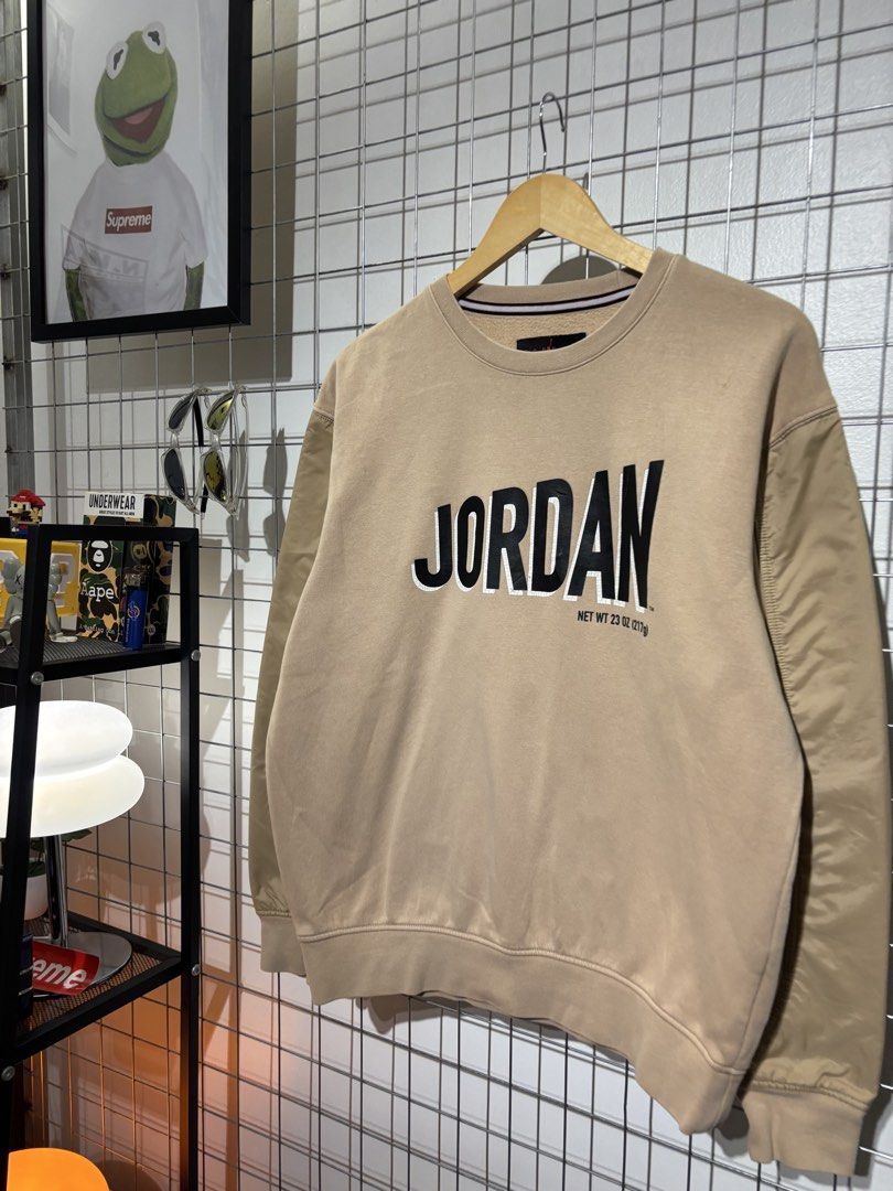 Jordan Beige Sweatshirt with Black Lettering (Category: Coats, Jackets and Outerwear) located in Cavite. Submitted by vlblgrmnts_ (Listing ID 1466076627, Image 3). Description: Jordan - P235 23x27 Bestfit Large 9/10 CR 900 Jordan crewneck sweatshirt in a tan beige colorway. Bold black JORDAN text printed on the chest along with a net weight detail. Ribbed collar featuring red and white stripes inside. Standard cuffs and hem. Classic piece for cas
