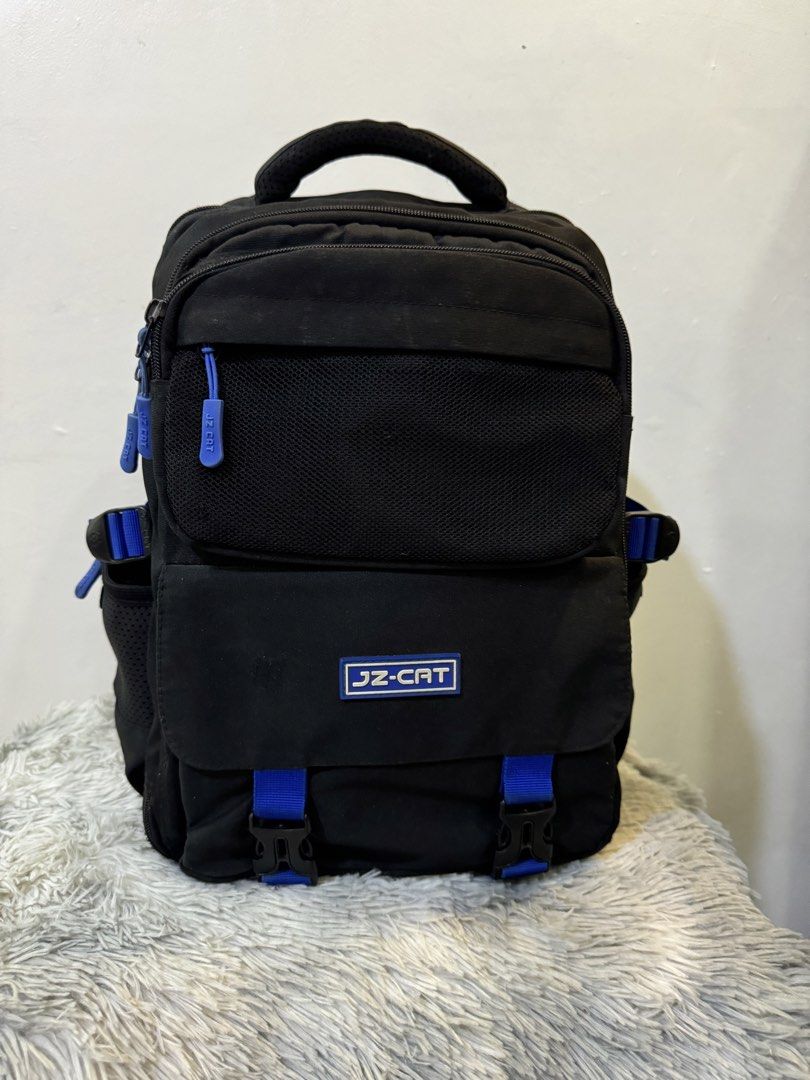 JZ-CAT Black and Blue Backpack (Category: Backpacks) located in Urdaneta. Submitted by kathleenja24136 (Listing ID 1465958334, Image 1). Description: - Color: Sleek black with eye-catching blue straps and zipper pulls - Storage: Main compartment, front pocket with mesh detail and buckle flap, and side mesh pockets for water bottles - Comfort: Padded shoulder straps and breathable mesh back panel - Portability: Sturdy top handle for easy grabbing 