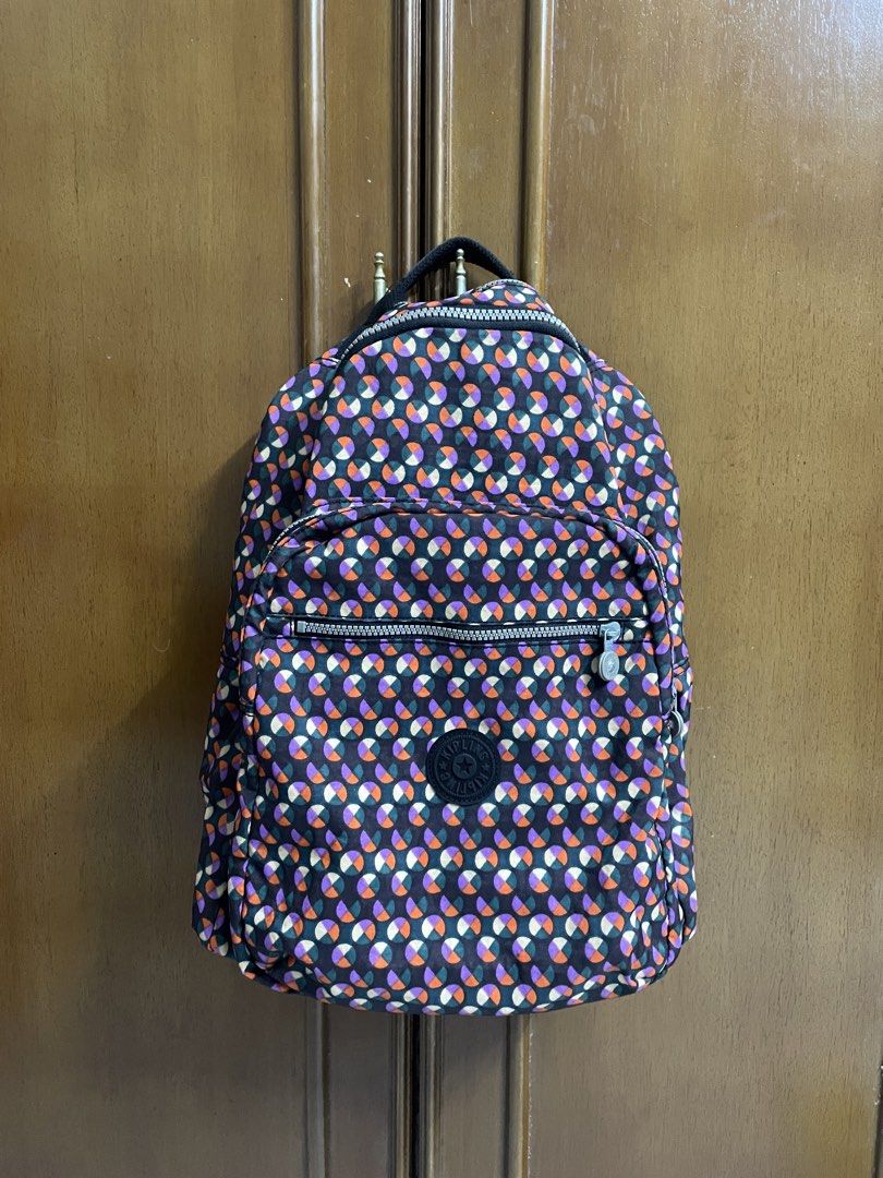 Kipling Backpack (Category: Backpacks) located in Kajang. Submitted by pumpyourdayyy (Listing ID 1466130376, Image 1). Description: - Brand: Kipling - Design: Colorful geometric circle pattern (purple, orange, green) with a dark exterior - Compartments: Zippered front pocket and heavy-duty double main zippers - Features: Sturdy black top handle and interior fabric tag - Condition: Excellent, perfect for daily wear or travel.