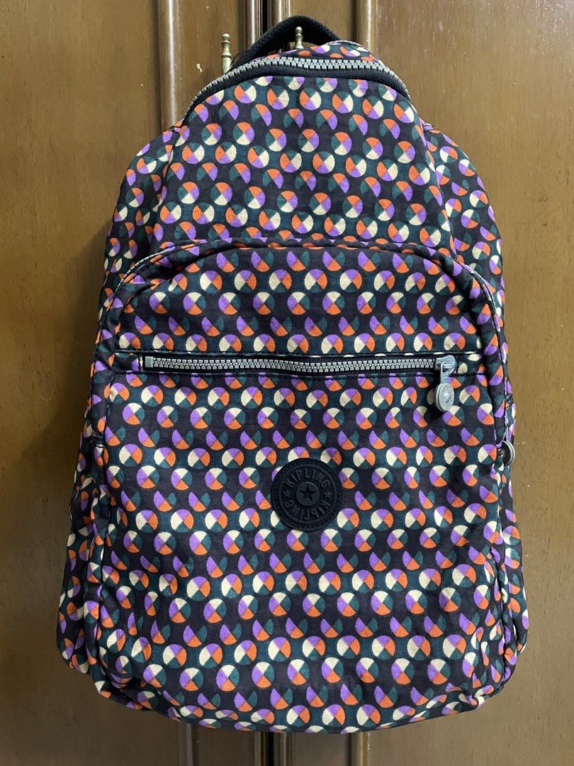 Kipling Backpack (Category: Backpacks) located in Kajang. Submitted by pumpyourdayyy (Listing ID 1466130376, Image 2). Description: - Brand: Kipling - Design: Colorful geometric circle pattern (purple, orange, green) with a dark exterior - Compartments: Zippered front pocket and heavy-duty double main zippers - Features: Sturdy black top handle and interior fabric tag - Condition: Excellent, perfect for daily wear or travel.