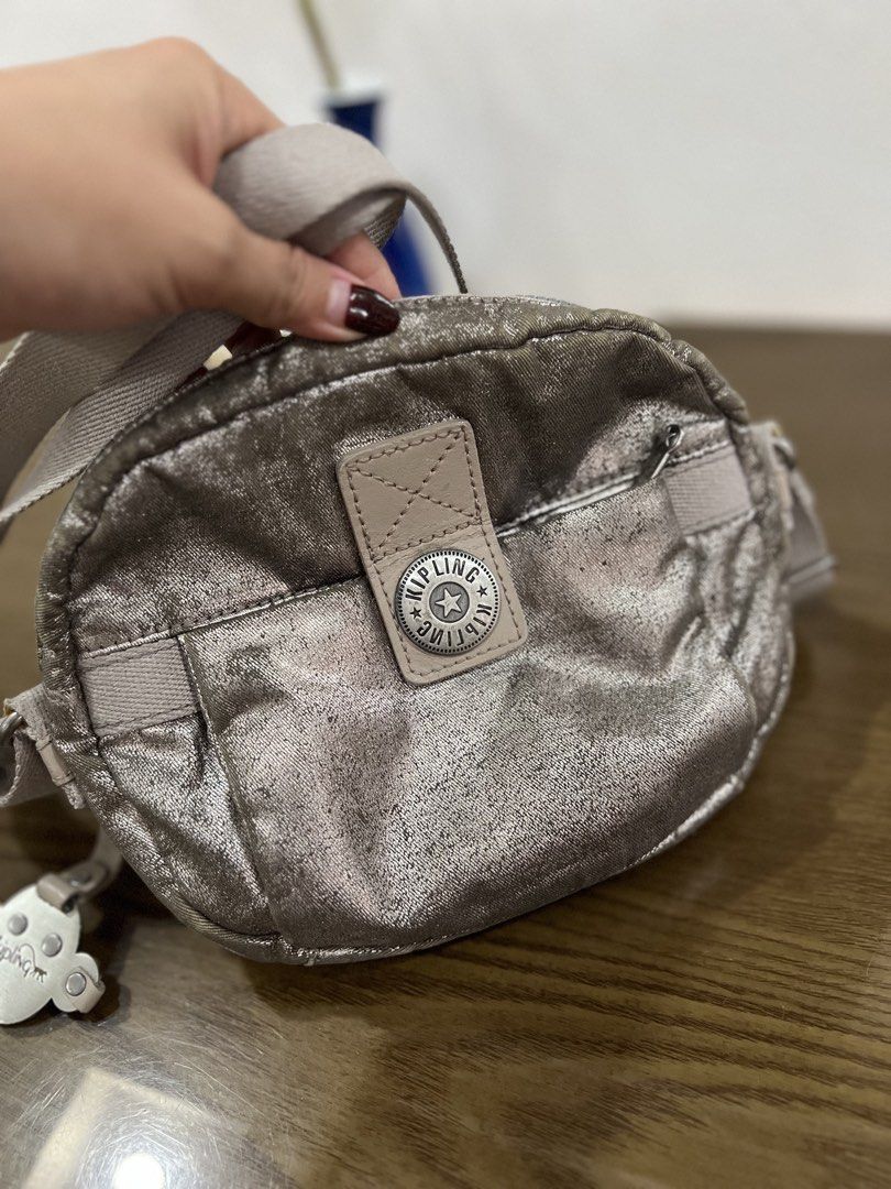 Kipling Metallic Silver Crossbody Bag with Monkey Keychain (Category: Cross-body Bags) located in Quezon City. Submitted by happyshop31 (Listing ID 1466098940, Image 1). Description: Kipling crossbody bag in a metallic silver finish. Compact round shape with a front zippered pocket and sturdy zip closure. Adjustable canvas strap in light grey. Includes the signature metal monkey keychain charm. Roomy interior for daily essentials. Minor scuffs on