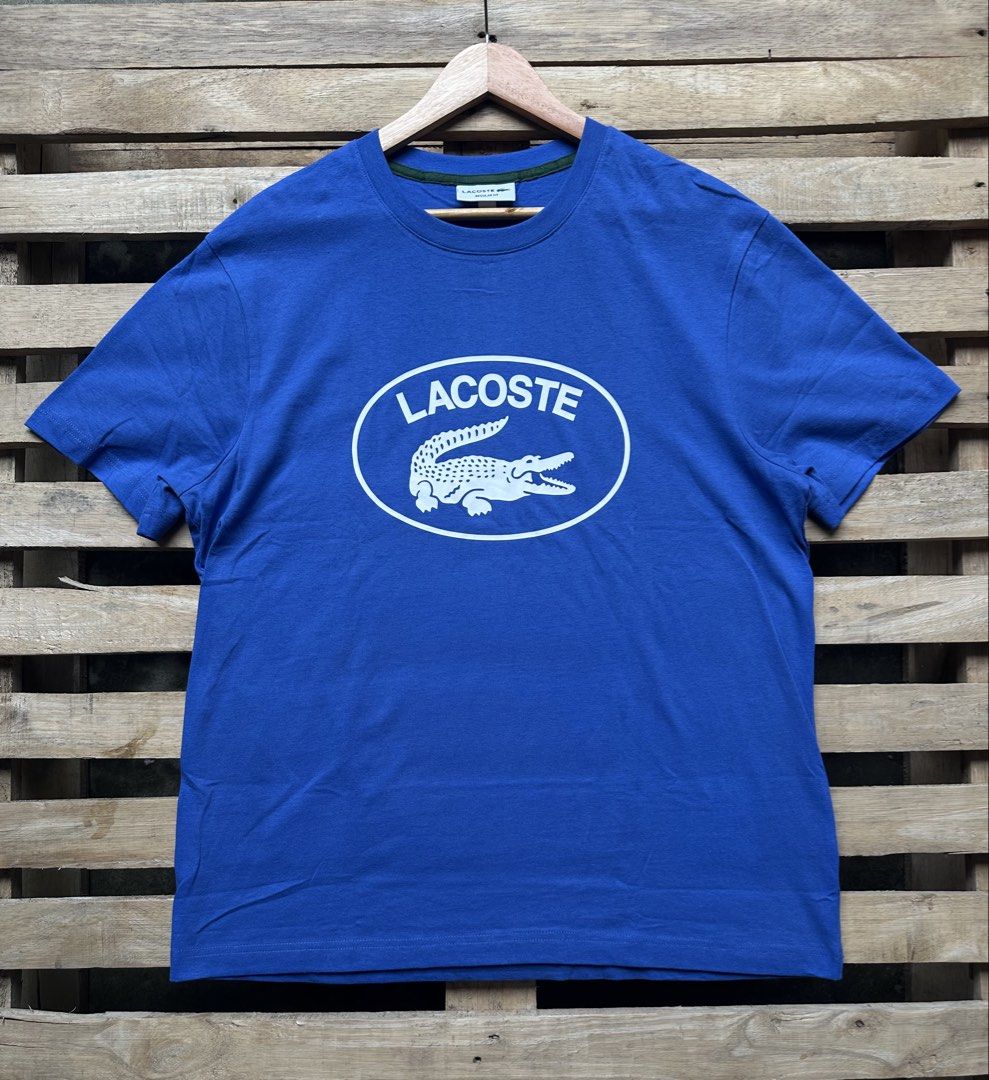 Lacoste Oval Logo Regular Fit T-Shirt Blue (Category: Tshirts & Polo Shirts ) located in Manila. Submitted by dough_lux (Listing ID 1466070138, Image 1). Description: - Brand: Lacoste - Style: Regular fit crew neck short sleeve t-shirt - Size: US XL / FR 6 - Color: Blue with a large white oval front graphic and branding - Details: Small green contrast trim inside collar and tiny embroidered crocodile logo near the back neckline - Condition: Excel