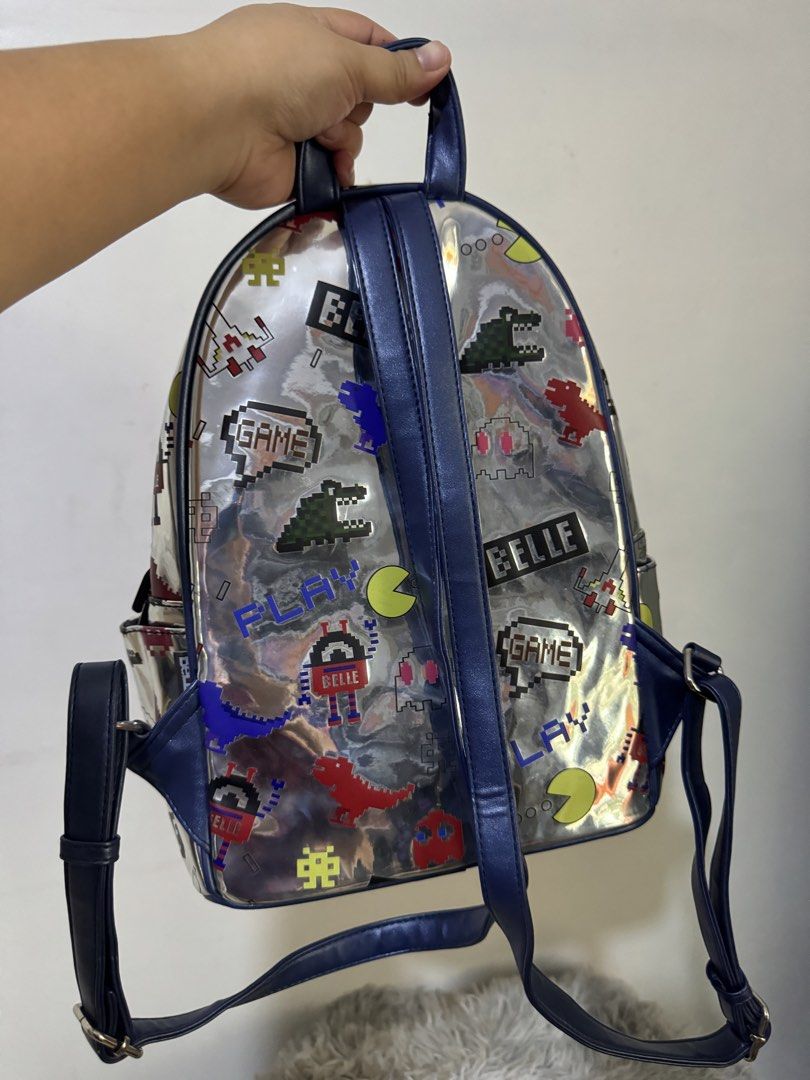 Metallic silver pixel retro arcade video game backpack (Category: Backpacks) located in Urdaneta. Submitted by kathleenja24136 (Listing ID 1465958921, Image 3). Description: - Metallic silver backpack with colorful retro arcade and pixel game graphics - Features Pac-Man ghosts, pixel dinosaurs, spaceships, and dark blue trim - Main compartment with double zippers and a front zipped pocket - Comfortable with adjustable shoulder straps and a top gr
