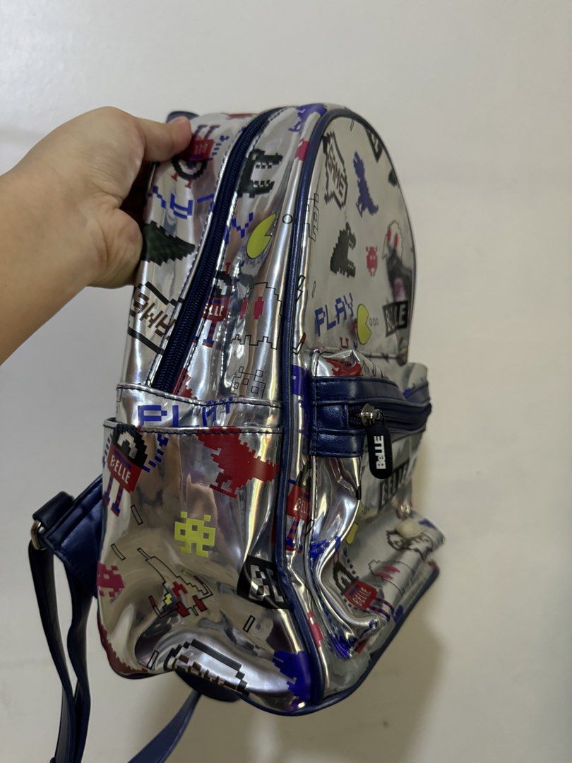 Metallic silver pixel retro arcade video game backpack (Category: Backpacks) located in Urdaneta. Submitted by kathleenja24136 (Listing ID 1465958921, Image 2). Description: - Metallic silver backpack with colorful retro arcade and pixel game graphics - Features Pac-Man ghosts, pixel dinosaurs, spaceships, and dark blue trim - Main compartment with double zippers and a front zipped pocket - Comfortable with adjustable shoulder straps and a top gr