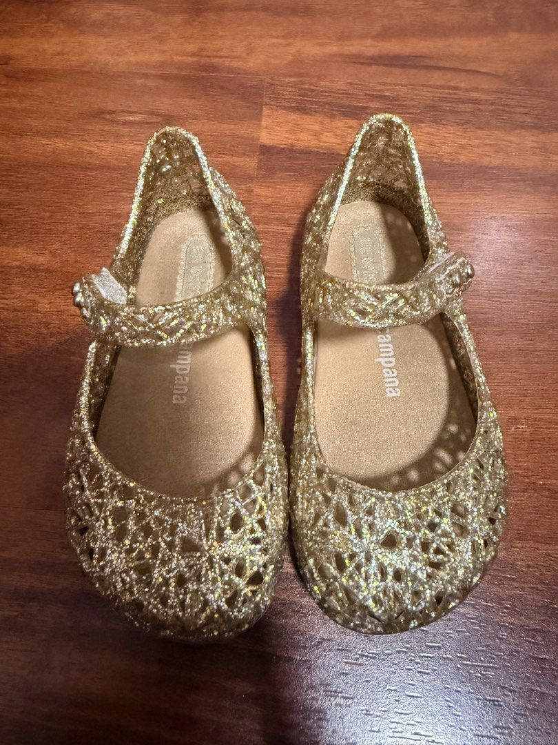 Mini Melissa + Campana Size 7 (Category: Babies & Kids Fashion) located in Cabanatuan. Submitted by baju101 (Listing ID 1466065170, Image 1). Description: - Authentic ❗️ - Brand: Mini Melissa - Style: Mary Jane jelly shoes - Color/Finish: Gold glitter with sparkly finish - Design: Cutout floral pattern across the toes - Closure: Adjustable button strap - Comfort: Cushioned tan insole and flat sole for daily wear.