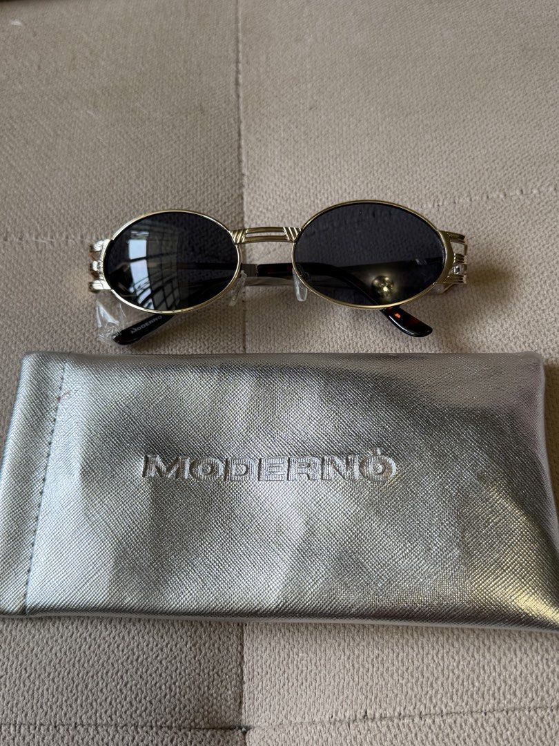 MODERNO Oval Sunglasses with Metallic Frame and Case (Category: Sunglasses & Eyewear) located in Pasig City. Submitted by miss_abuelita (Listing ID 1465977927, Image 3). Description: - Brand: MODERNO - Style: Oval sunglasses with dark tint - Frame: Gold-tone metallic with unique geometric side details and branded temples - Condition: Unused and brand new (protective wrapping still attached on the arm) - Inclusions: Matching silver textured case w