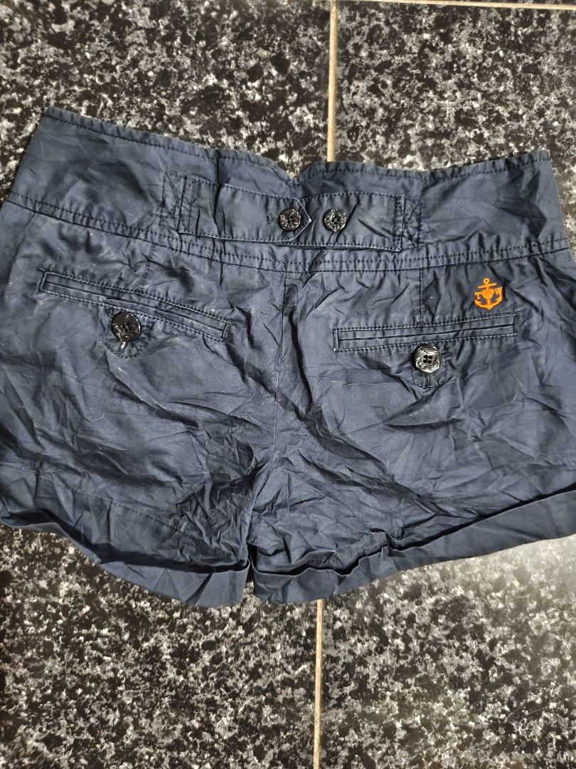 Navy blue cuffed shorts with button details (Category: Shorts) located in Manila. Submitted by sunnysideup.tree (Listing ID 1466028092, Image 2). Description: - Color: Navy blue - Fit: High-waisted with rolled-up cuffs - Details: Multiple front buttons, cute bear graphic on the front right, and anchor logo embroidery on the back right pocket - Interior: Stylish orange and white checkered waistband lining - Pockets: Functional front and back pocke